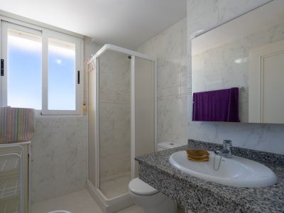Salle de bain fonctionnelle avec carrelage mural effet marbre blanc, meuble-lavabo en granit moucheté et lavabo ovale. Comprend une cabine de douche d'angle et fenêtre.