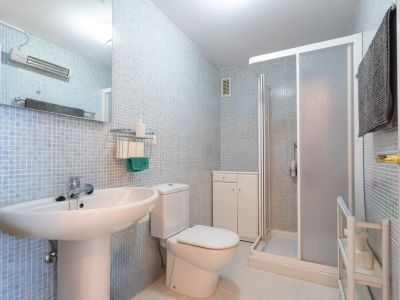 Salle de bain fonctionnelle avec murs en mosaïque bleu clair, lavabo sur pied, toilettes, cabine de douche vitrée dépolie et meuble de rangement blanc.