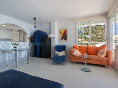 Séjour-salle à manger lumineux avec carrelage clair, table en verre et canapé orange. Grandes baies vitrées offrant une vue sur la colline verdoyante.