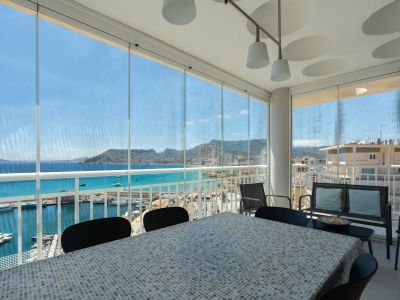 Terrasse vitrée avec espace repas, offrant des vues directes sur le port de Calpe, la mer turquoise et l'emblématique Peñón de Ifach.