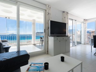 Vaste salon carrelé avec meuble TV et canapé, s'ouvrant sur une terrasse vitrée offrant une vue mer panoramique et un plafond à motifs circulaires.