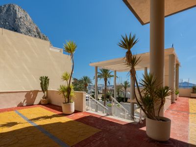 Vaste terrasse extérieure avec carrelage rouge et jaune, plantes méditerranéennes, offrant une vue directe sur le port de Calpe et le Peñón de Ifach sous un ciel bleu.