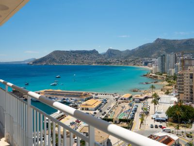Vue panoramique depuis la terrasse sur le port de Calpe, la baie aux eaux turquoise et le littoral avec montagnes.