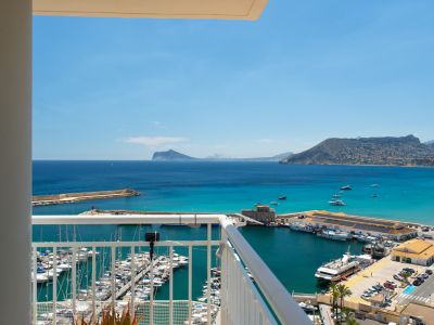 Vue panoramique depuis le balcon sur la marina de Calpe, ses yachts, la baie aux eaux turquoise et les montagnes côtières lointaines sous un ciel clair.