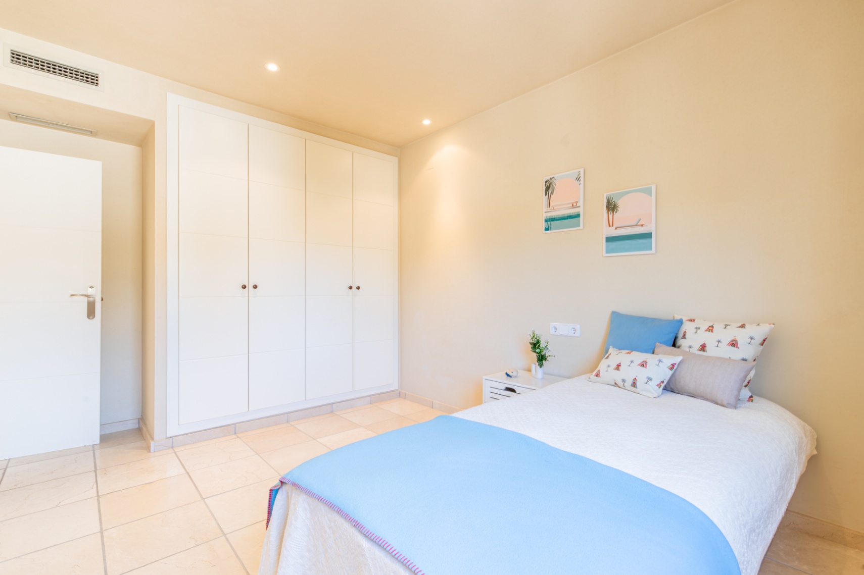 Chambre lumineuse dotée de vastes placards intégrés blancs, d'un sol carrelé clair et d'un lit confortable avec décoration côtière. Éclairage encastré.