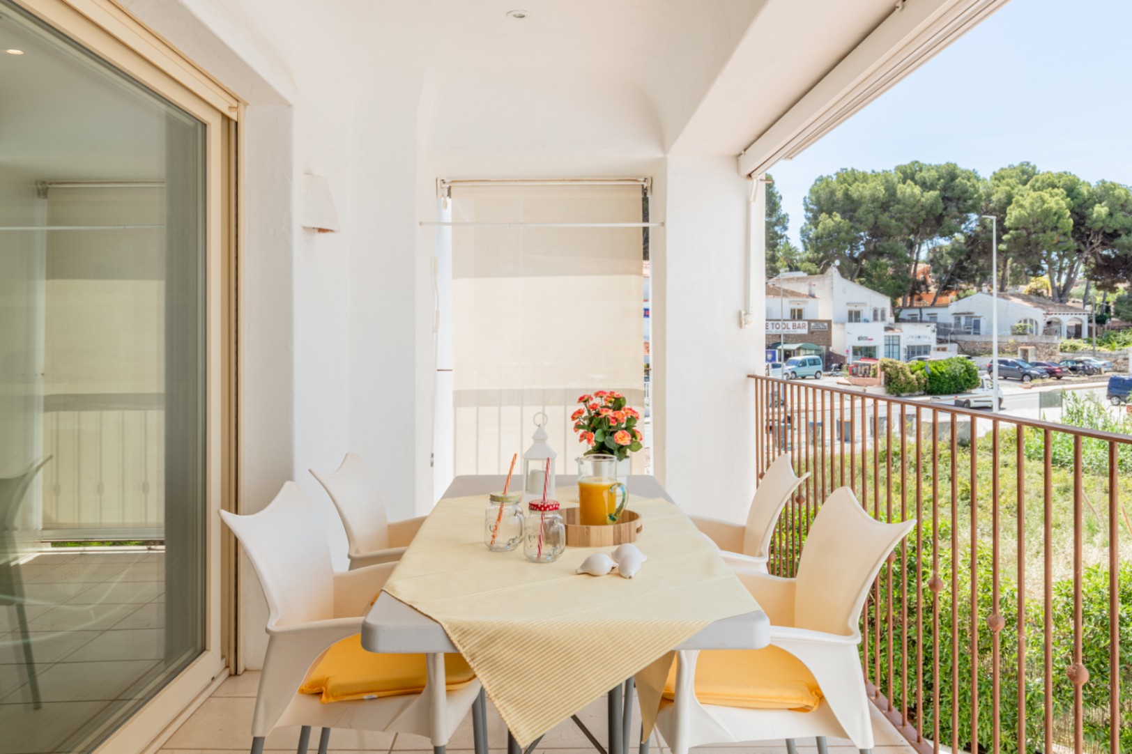 Lumineuse terrasse privée avec table à manger pour quatre, offrant des vues sur la rue et la verdure, accessible par une grande porte coulissante vitrée.