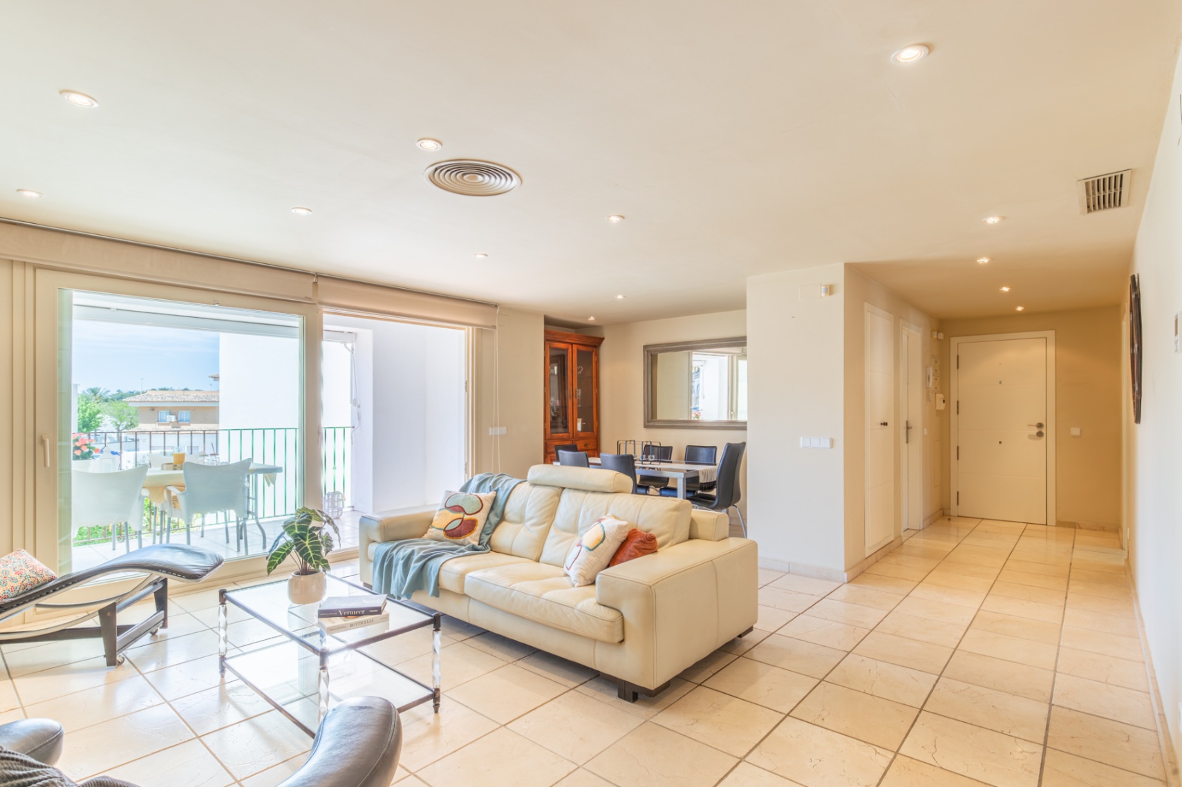 Vaste salon-salle à manger décloisonné avec canapé en cuir crème, accès direct à une terrasse privée, baigné de lumière naturelle et carrelage clair au sol.