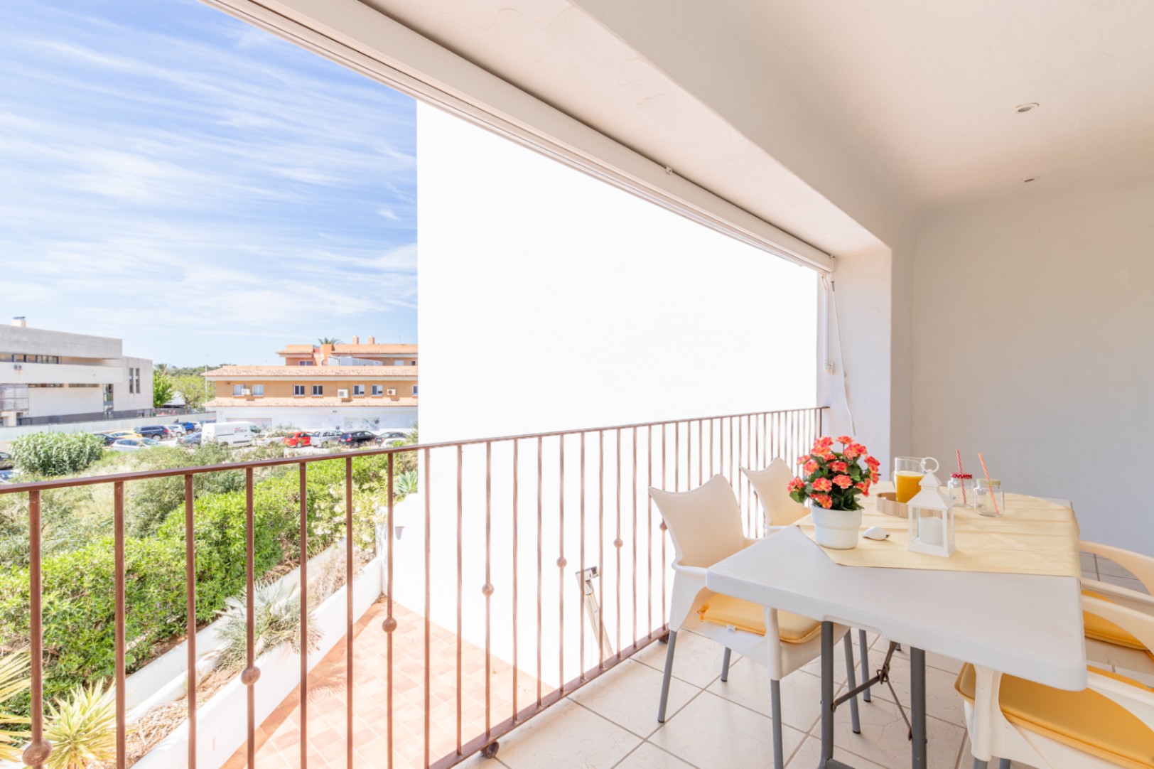 Vaste terrasse privée carrelée avec balustrade métallique, aménagée avec une table et des chaises pour les repas en plein air. Vues sur la verdure et l'architecture locale.