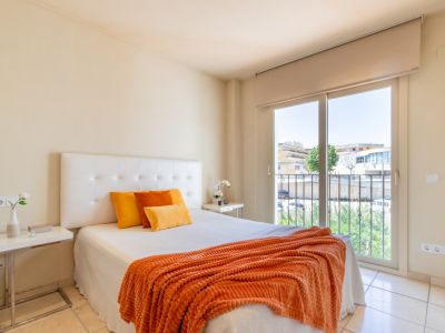 Chambre lumineuse avec lit double, tête de lit capitonnée, sol carrelé clair et accès direct à un balcon offrant des vues urbaines.