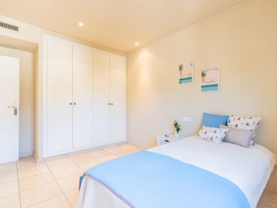Chambre lumineuse dotée de vastes placards intégrés blancs, d'un sol carrelé clair et d'un lit confortable avec décoration côtière. Éclairage encastré.