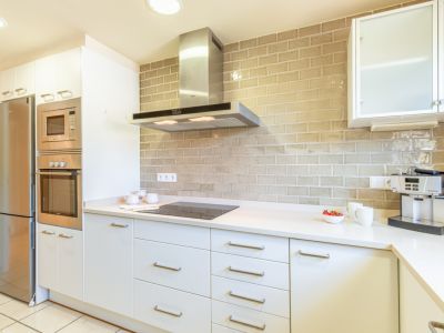 Cuisine contemporaine avec des armoires blanches épurées, des appareils encastrés en acier inoxydable et un dosseret distinctif en carrelage beige effet brique.