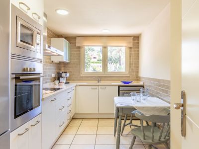 Cuisine fonctionnelle avec électroménager intégré en acier inoxydable, plan de travail clair et crédence en briques. Comprend une table compacte et une fenêtre sur verdure.