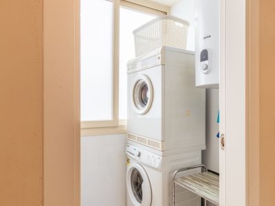 Espace buanderie compact avec lave-linge et sèche-linge superposés, optimisant l'espace. Chauffe-eau intégré et fenêtre dépolie pour une lumière naturelle.