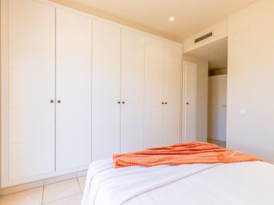 Grande armoire encastrée aux portes blanches à panneaux et poignées sombres, offrant un rangement généreux dans cette chambre lumineuse avec carrelage au sol.