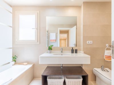 Salle de bain complète avec meuble-lavabo suspendu, vasque intégrée et grand miroir. Carrelage beige clair, fenêtre discrète et baignoire encastrée.