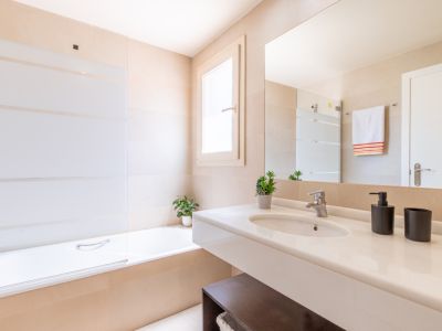 Salle de bain moderne avec meuble-lavabo flottant blanc, grand miroir et baignoire avec pare-douche en verre rayé, sur des murs carrelés neutres.