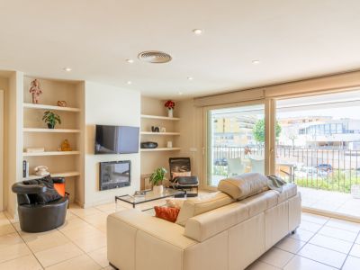 Salon lumineux avec canapé crème, carrelage et étagères intégrées autour d'une cheminée et TV. De larges baies vitrées s'ouvrent sur une terrasse privée avec vue urbaine.