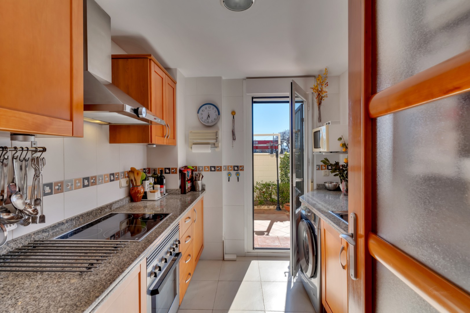Cuisine fonctionnelle avec des armoires en bois clair, des plans de travail en granit et des appareils en acier inoxydable. Accès direct à un patio extérieur.