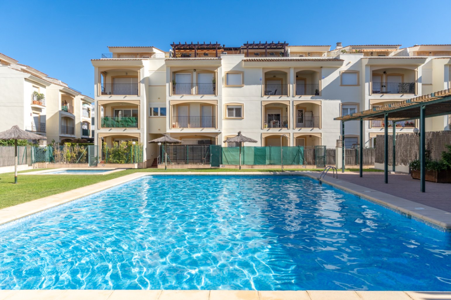 Vaste piscine communautaire d'eau salée, bordée d'une pelouse verdoyante et des bâtiments d'appartements crème avec balcons privés.
