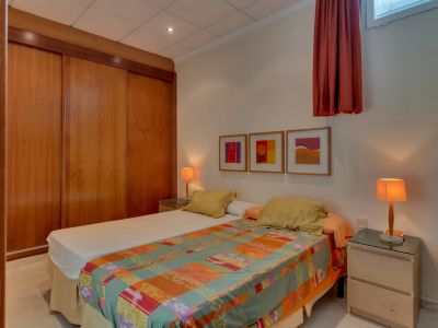 Chambre avec deux lits simples, une grande armoire encastrée en bois à portes coulissantes et deux tables de chevet avec lampes chaleureuses. Art abstrait sur le mur blanc.
