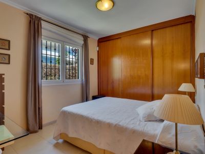 Chambre avec lit double, armoire intégrée en bois et fenêtre grillagée donnant sur la verdure extérieure.