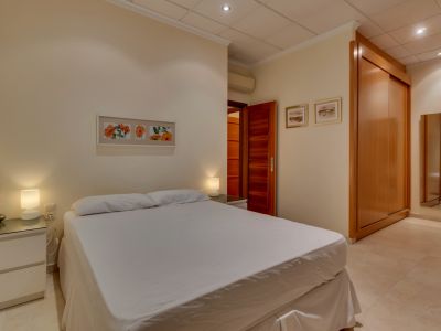 Chambre confortable avec lit double, tables de chevet modernes, grande armoire encastrée en bois et carrelage clair, équipée de la climatisation.