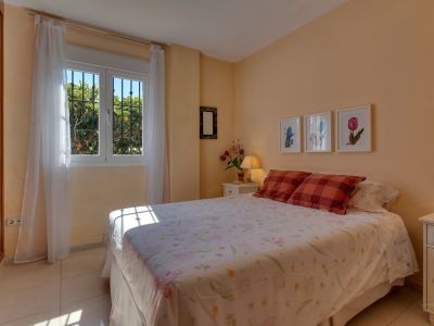 Chambre lumineuse aux murs couleur pêche, avec un lit double et une fenêtre à barreaux offrant une vue sur le jardin et une lumière naturelle abondante. Armoire intégrée.