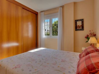 Chambre principale lumineuse avec grande armoire intégrée en bois clair, lit double et fenêtre sécurisée offrant une vue sur la verdure.