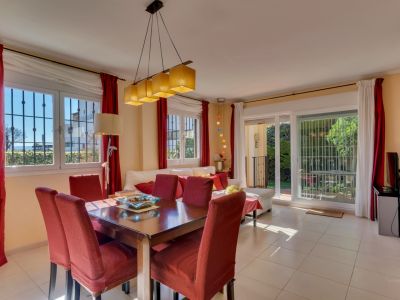 Grand salon-salle à manger avec table en bois pour six, chaises rouges et lumière naturelle abondante. Accès direct au jardin par des portes coulissantes vitrées.
