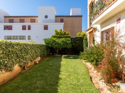 Jardin privé avec pelouse bien entretenue, entouré de haies verdoyantes et d'un petit arbre fruitier. Des bâtiments modernes et une façade avec auvent sont visibles en arrière-plan.