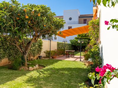 Jardin privé avec pelouse, néflier fruité et haies. Patio pavé avec table en bois, ombragé par un auvent orange rétractable. Éclairage extérieur et bougainvilliers roses ajoutent au charme.