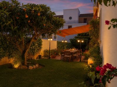 Jardin privé éclairé au crépuscule, avec un néflier, une table à manger extérieure sous un store orange et une végétation luxuriante.