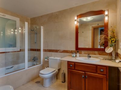 Salle de bain avec carrelage beige clair et bande de marbre, baignoire avec pare-douche vitré, et meuble-lavabo en bois avec miroir éclairé. Une fenêtre dépolie assure l'intimité.