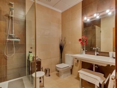 Salle de bain complète avec douche vitrée, carrelage beige et marron, lavabo suspendu et miroir avec éclairage moderne.