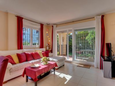 Salon lumineux avec canapé blanc, coussins colorés, sol carrelé et accès direct au jardin privé par des portes coulissantes vitrées.