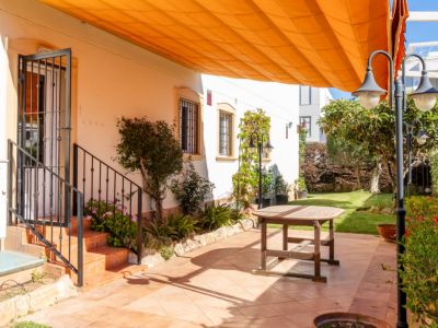 Vaste patio extérieur carrelé de terre cuite, avec une table en bois et un grand store orange rétractable. Accès direct à la maison et au jardin verdoyant.