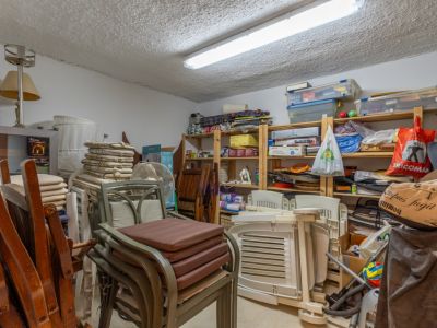 Vaste pièce de rangement avec de grandes étagères en bois remplies d'articles ménagers variés, des meubles de jardin empilés et un éclairage fluorescent au plafond.