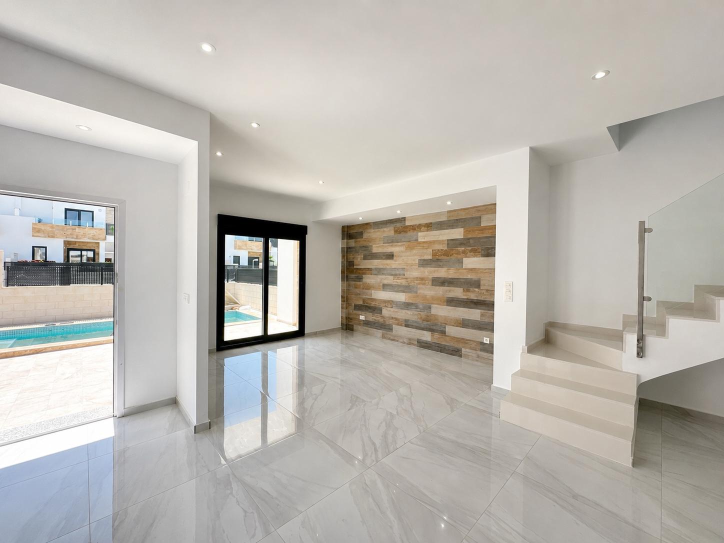 Grand espace de vie avec carrelage en porcelaine polie, mur décoratif à panneaux effet bois et accès direct à la piscine privée. Escalier moderne avec garde-corps en verre.