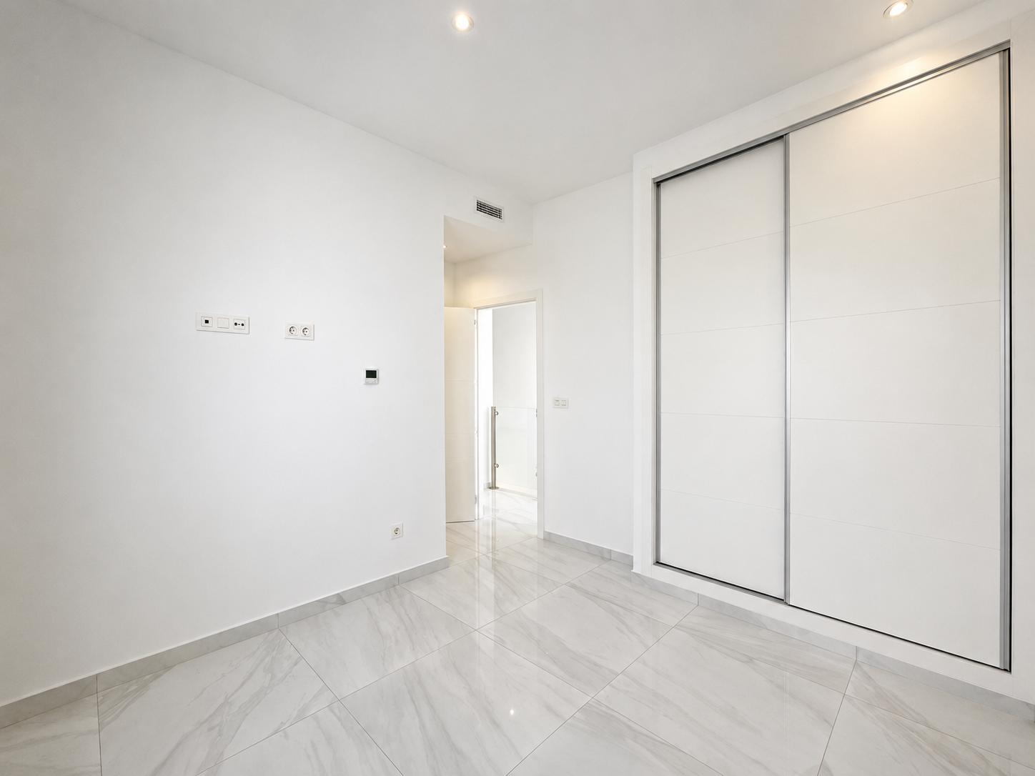 Pièce moderne avec de grandes armoires coulissantes encastrées blanches, un sol carrelé effet marbre gris clair et des spots encastrés. Un design épuré et fonctionnel.