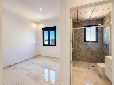 Chambre spacieuse au sol clair effet marbre et fenêtre foncée offrant des vues lointaines, attenante à une salle de bain avec douche et carrelage mural géométrique.