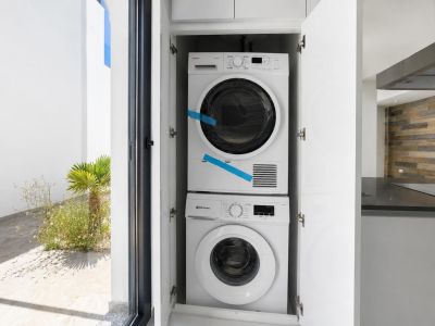 Espace buanderie intégré avec lave-linge et sèche-linge superposés, discrètement dissimulés dans une armoire blanche. Aperçu du jardin extérieur et de la cuisine moderne.