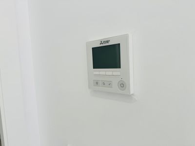 Panneau de commande Mitsubishi Electric pour climatisation gainable, avec écran numérique et boutons intuitifs, intégré au mur blanc.