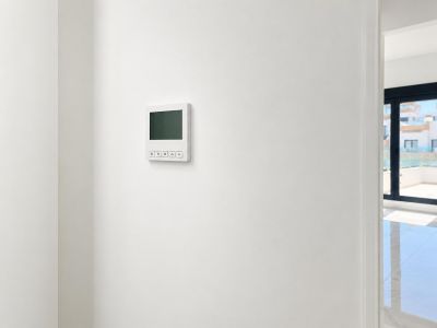 Panneau de commande numérique moderne pour la climatisation sur un mur blanc épuré, jouxtant un espace lumineux avec grandes baies vitrées et carrelage brillant.