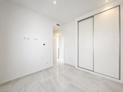 Pièce moderne avec de grandes armoires coulissantes encastrées blanches, un sol carrelé effet marbre gris clair et des spots encastrés. Un design épuré et fonctionnel.