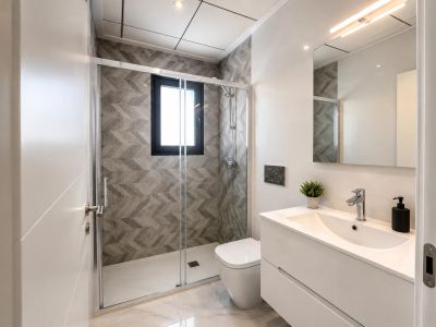 Salle de bain contemporaine avec douche à l'italienne, paroi vitrée, carrelage mural géométrique gris et fenêtre. Meuble-lavabo blanc suspendu sur sol effet marbre.