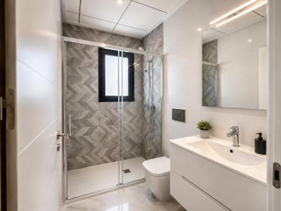 Salle de bain moderne avec douche à l'italienne, carrelage gris géométrique et fenêtre. Meuble-lavabo blanc, miroir éclairé par LED et sol effet marbre.