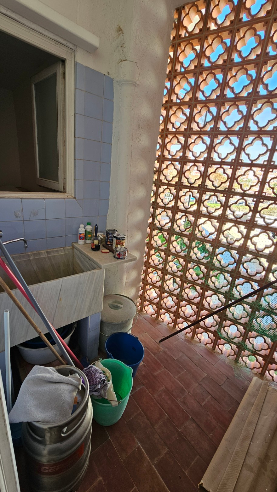 Espace utilitaire avec un grand évier en marbre, carrelage mural bleu et claustra en terre cuite filtrant la lumière naturelle. Potentiel de rénovation.
