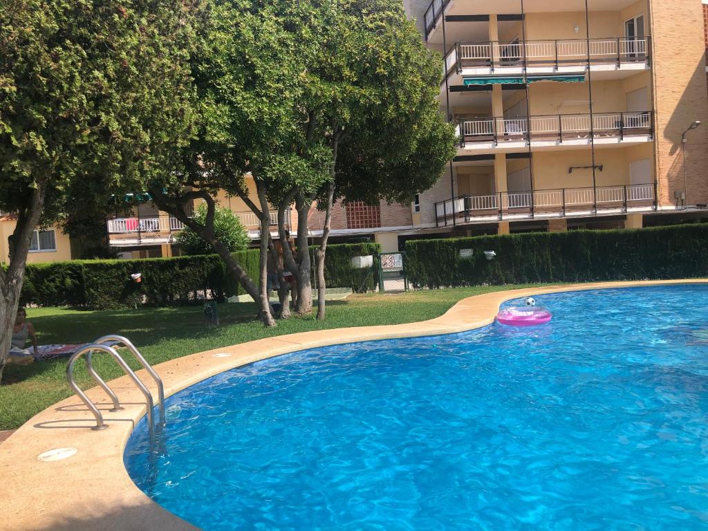 Piscine communautaire avec bord incurvé en béton et escaliers métalliques, entourée d'une pelouse et d'arbres. Bâtiment résidentiel à plusieurs étages avec balcons en arrière-plan.