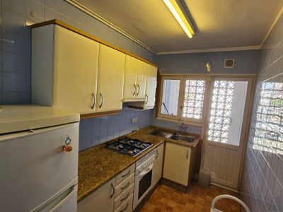 Cuisine fonctionnelle avec carrelage bleu, plan de travail effet granit et meubles blancs. Équipée d'une plaque de cuisson à gaz, d'un four et d'une fenêtre à motifs.