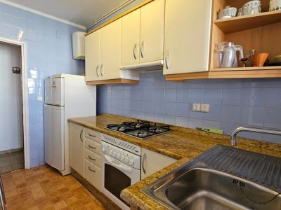 Cuisine fonctionnelle avec carrelage mural bleu clair, plan de travail effet granit et armoires blanches. Équipée d'une plaque de cuisson à gaz, four, évier en inox et réfrigérateur.